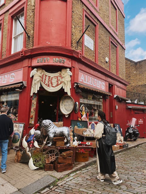 The image depicts a red, historic retail storefront with large display windows, located on a busy street during daytime. The shop's name, 'ALICE'S,' is prominently displayed on a sign above the window